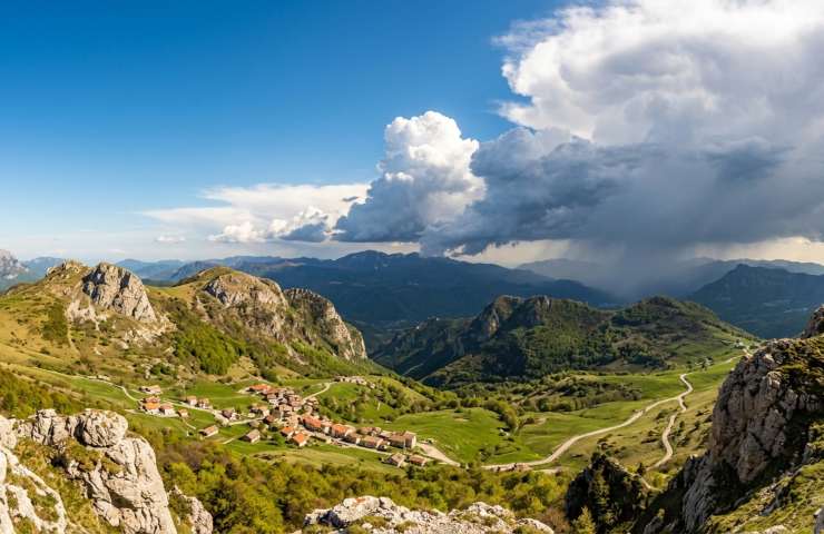 Fronte temporalesco in arrivo sulle Alpi e borgo montano soleggiato, previsioni meteo instabilità Nord Italia aprile 2026.