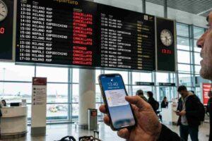 Tabellone voli cancellati in aeroporto italiano per sciopero aereo 10 aprile 2026 con passeggero che controlla notifiche su smartphone.